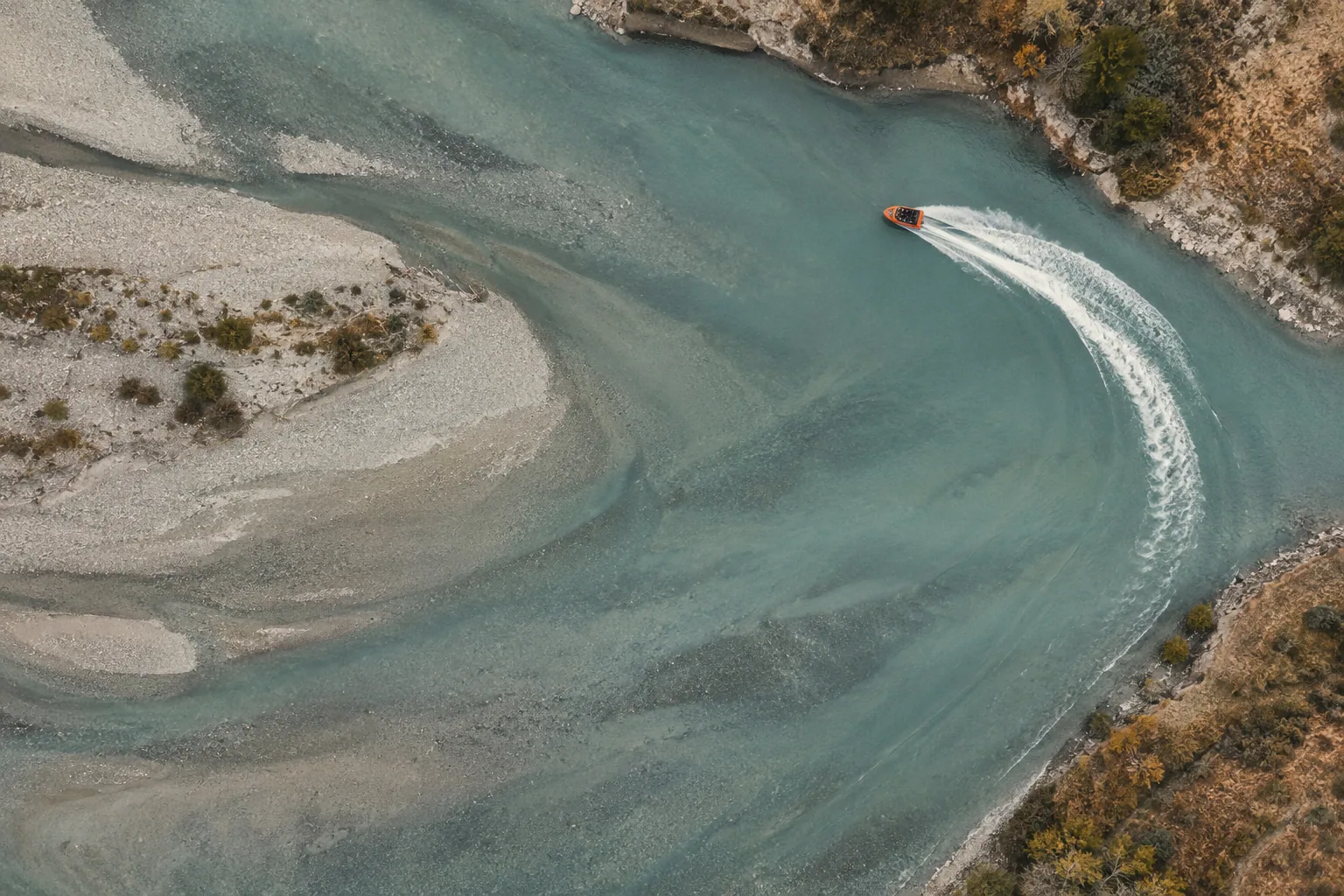 An orange jet boat turns through a turquoise braided river